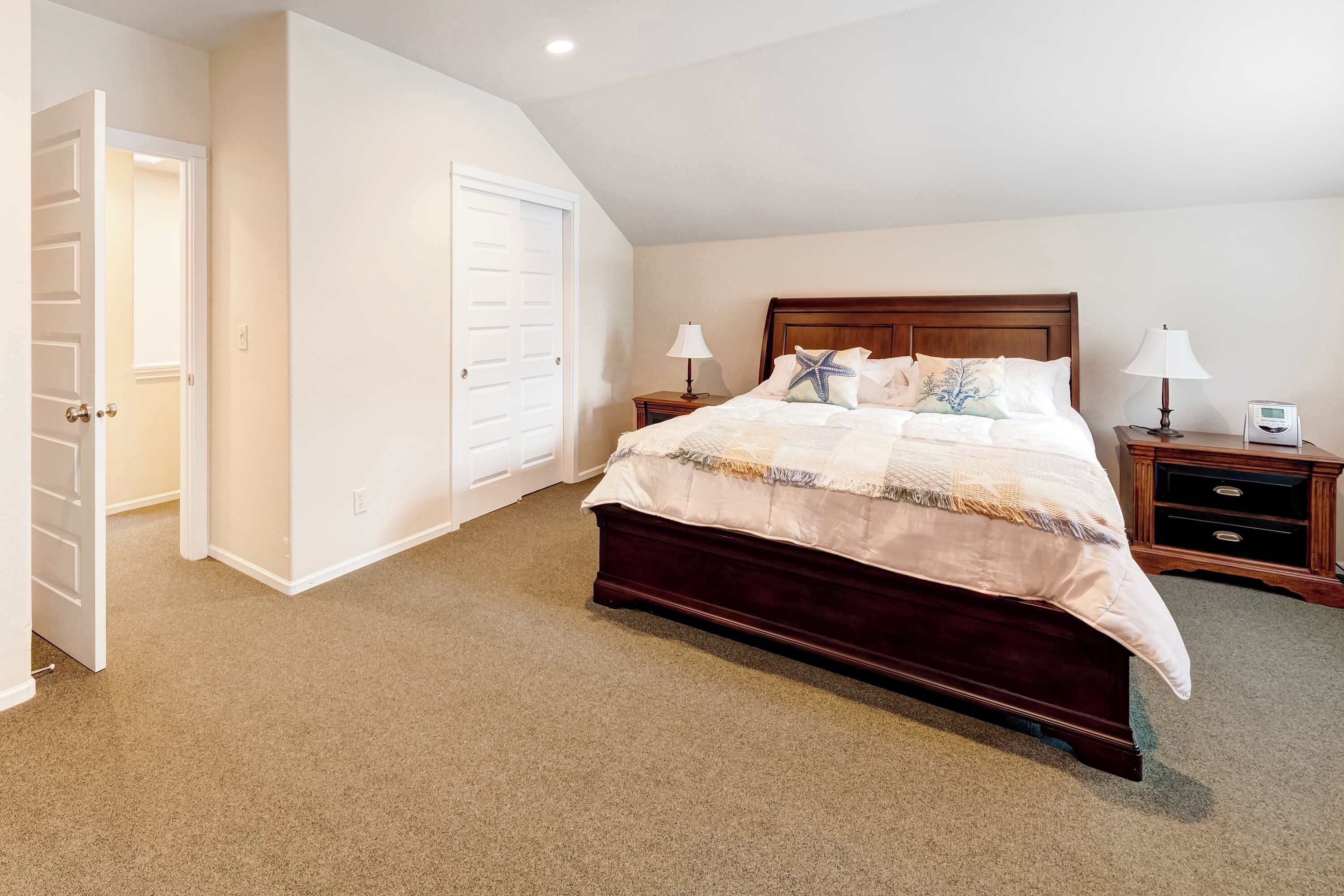 A bedroom with a large bed, two bedside tables with lamps, a wooden headboard, and a closet with a door.