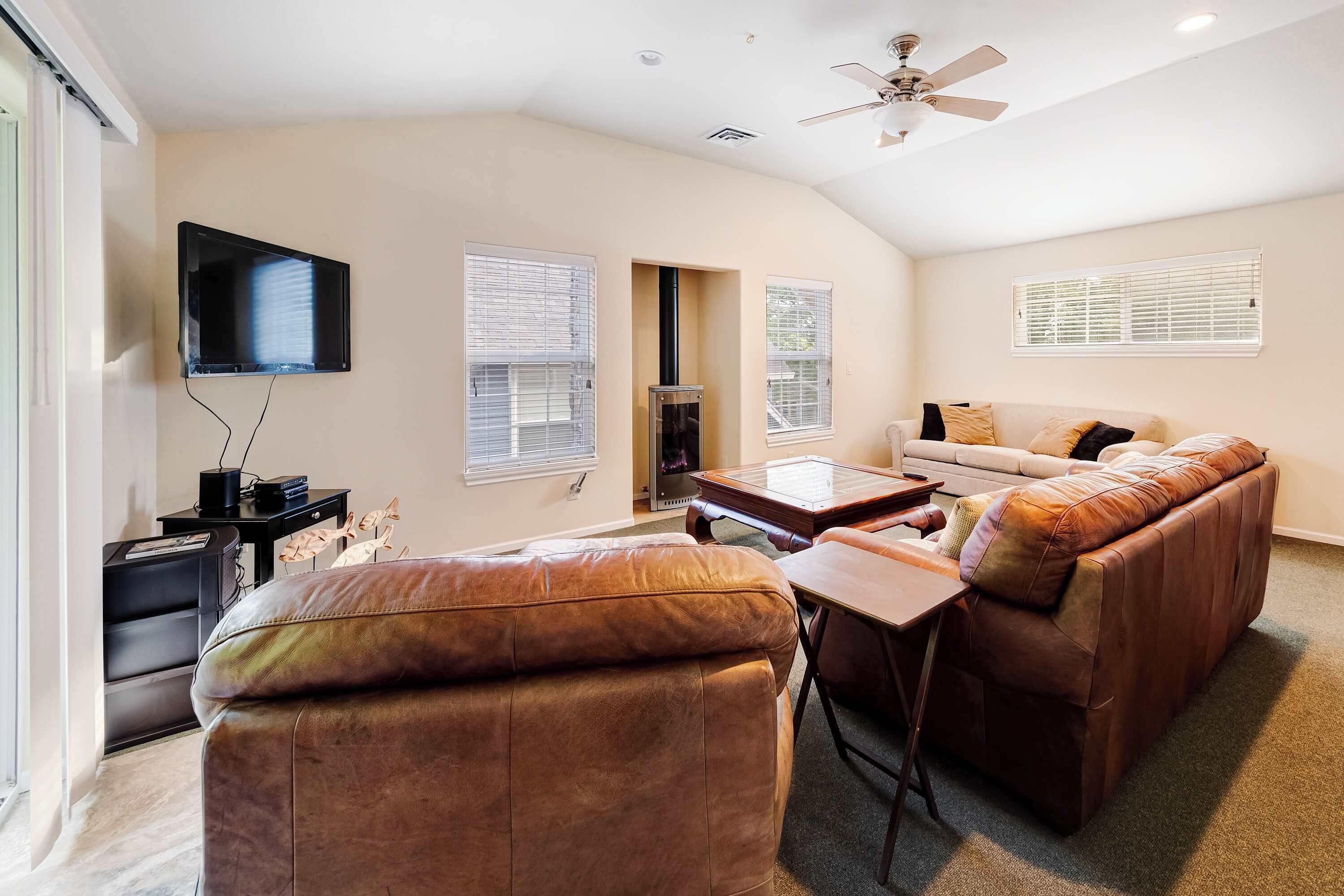 A living room with a sofa, a coffee table, a TV mounted on the wall, and a ceiling fan.