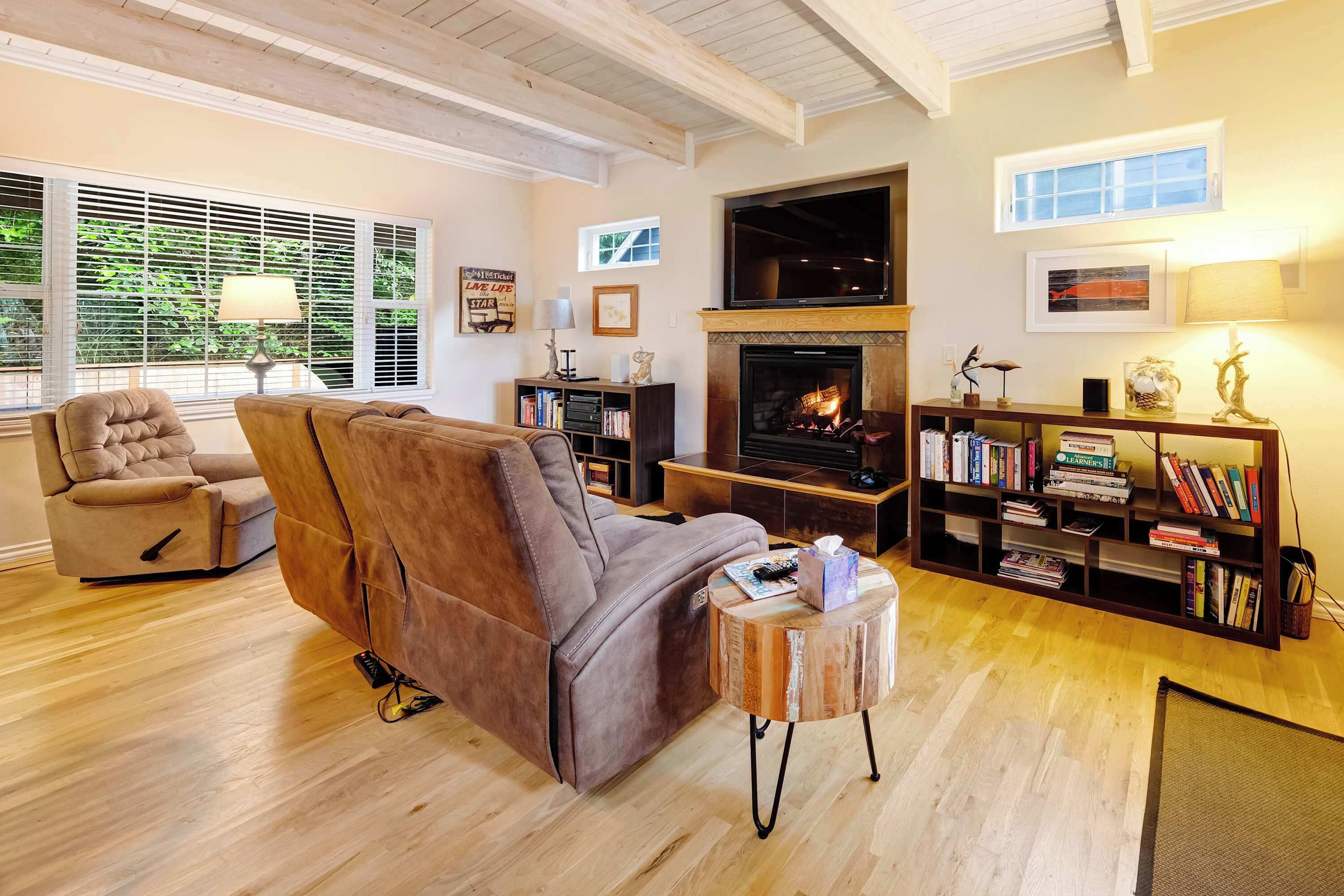 A cozy living room with a fireplace, a sofa, a bookshelf, and a window with blinds.