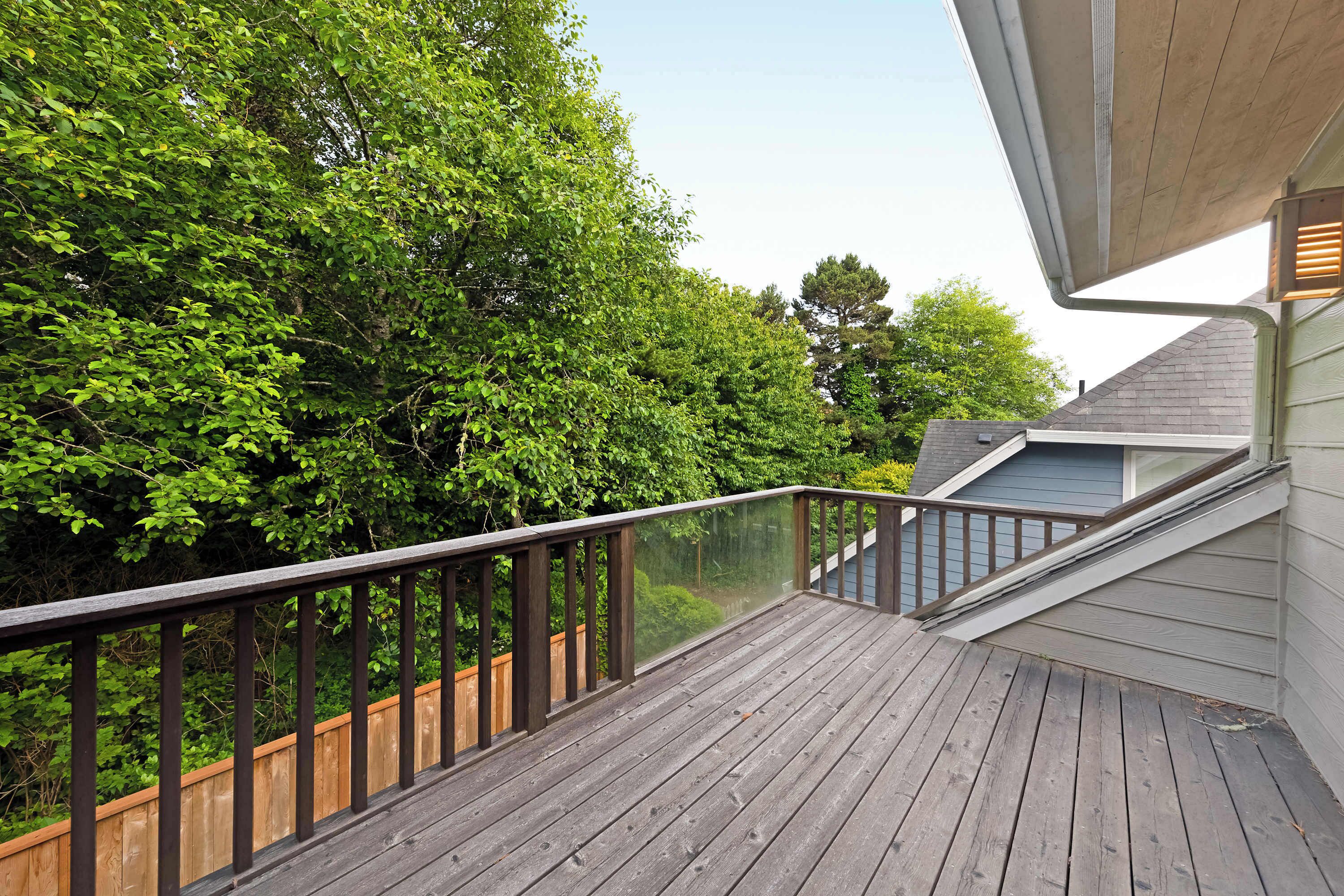 Um deck de madeira com guarda-corpo de vidro, com vista para uma área verde exuberante.