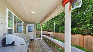 Une terrasse extérieure couverte, équipée d’un barbecue, de rampes en bois et offrant une vue sur une zone boisée.