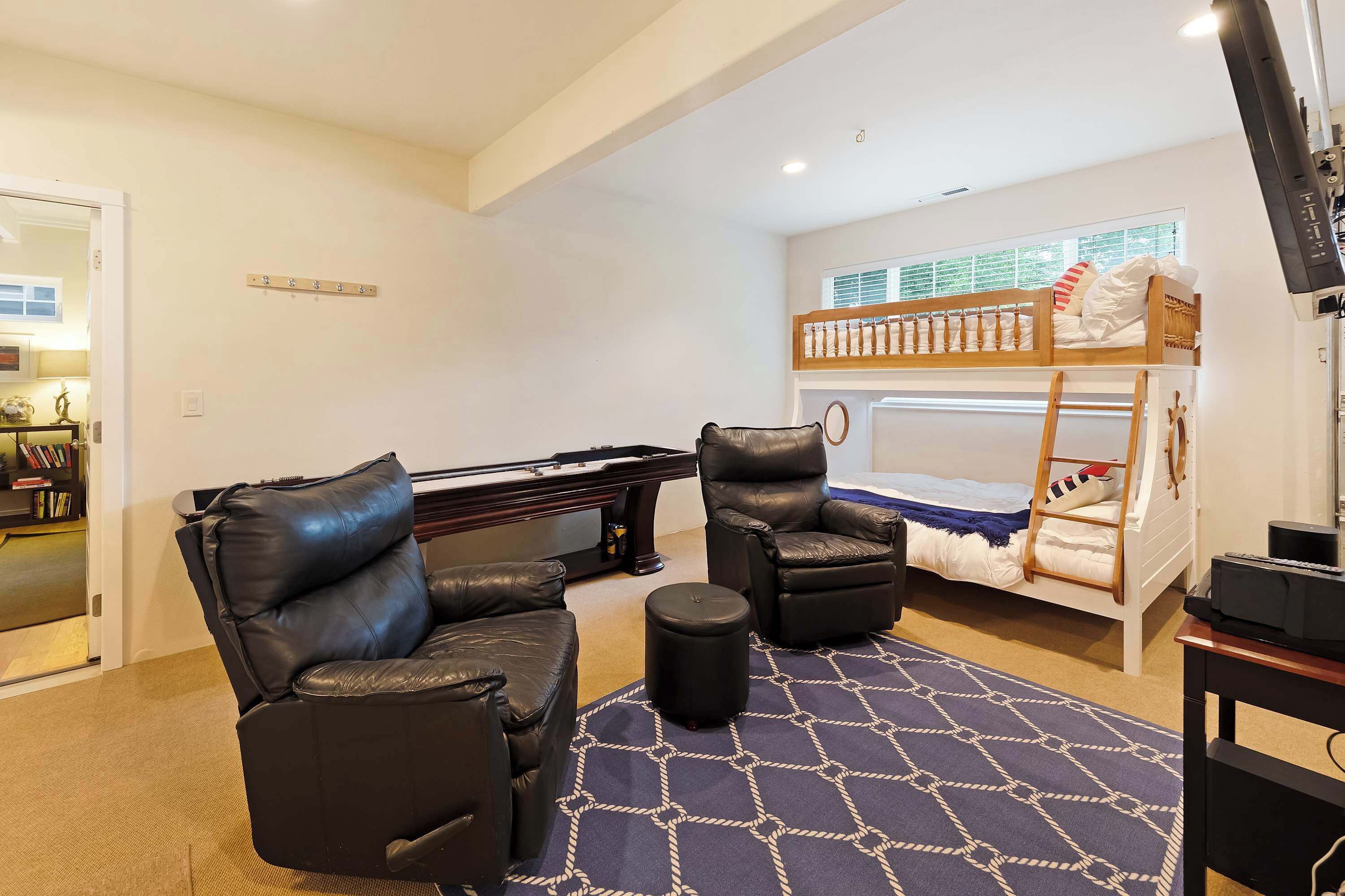 A room with a bunk bed, a pool table, two leather chairs, and a small ottoman.