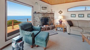Una sala de estar acogedora con chimenea de piedra, vista al océano, sofá a rayas y un sillón color turquesa.