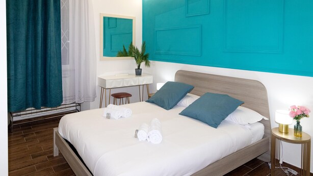 A hotel room with a bed, a desk, a chair, a potted plant, and a nightstand with a lamp and flowers. - San Giovanni prestige flat by RHR (Roma)