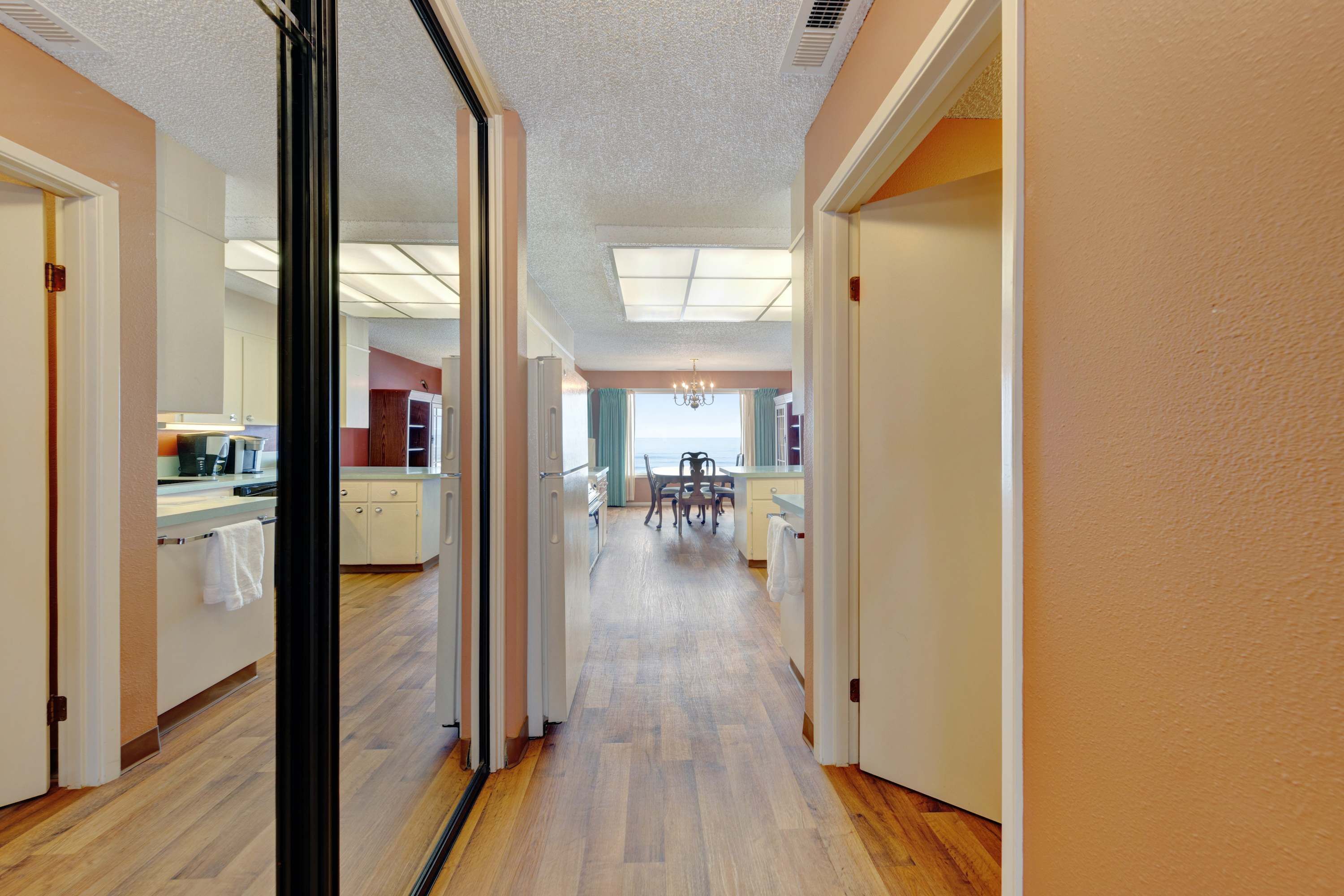 A hallway with wooden flooring, white walls, and a view into a dining area with a table and chairs.