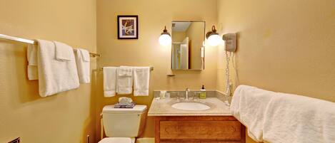 A bathroom with a toilet, sink, and wooden vanity. There are towels hanging on the wall and a framed picture above the mirror.