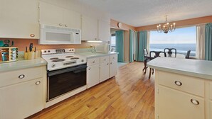 A kitchen with a stove, microwave, and wooden flooring. - Lovely oceanfront condo with sweeping water views and balcony (Gleneden Beach)