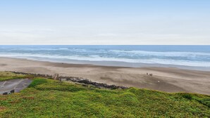 A beach with a rocky shoreline, a few people walking, and a clear sky. - Lovely oceanfront condo with sweeping water views and balcony (Gleneden Beach)