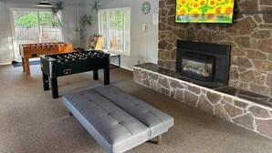 A cozy living room with a foosball table, a comfortable grey sofa, a stone fireplace, and a TV mounted on the wall. - Lovely oceanfront condo with sweeping water views and balcony (Gleneden Beach)