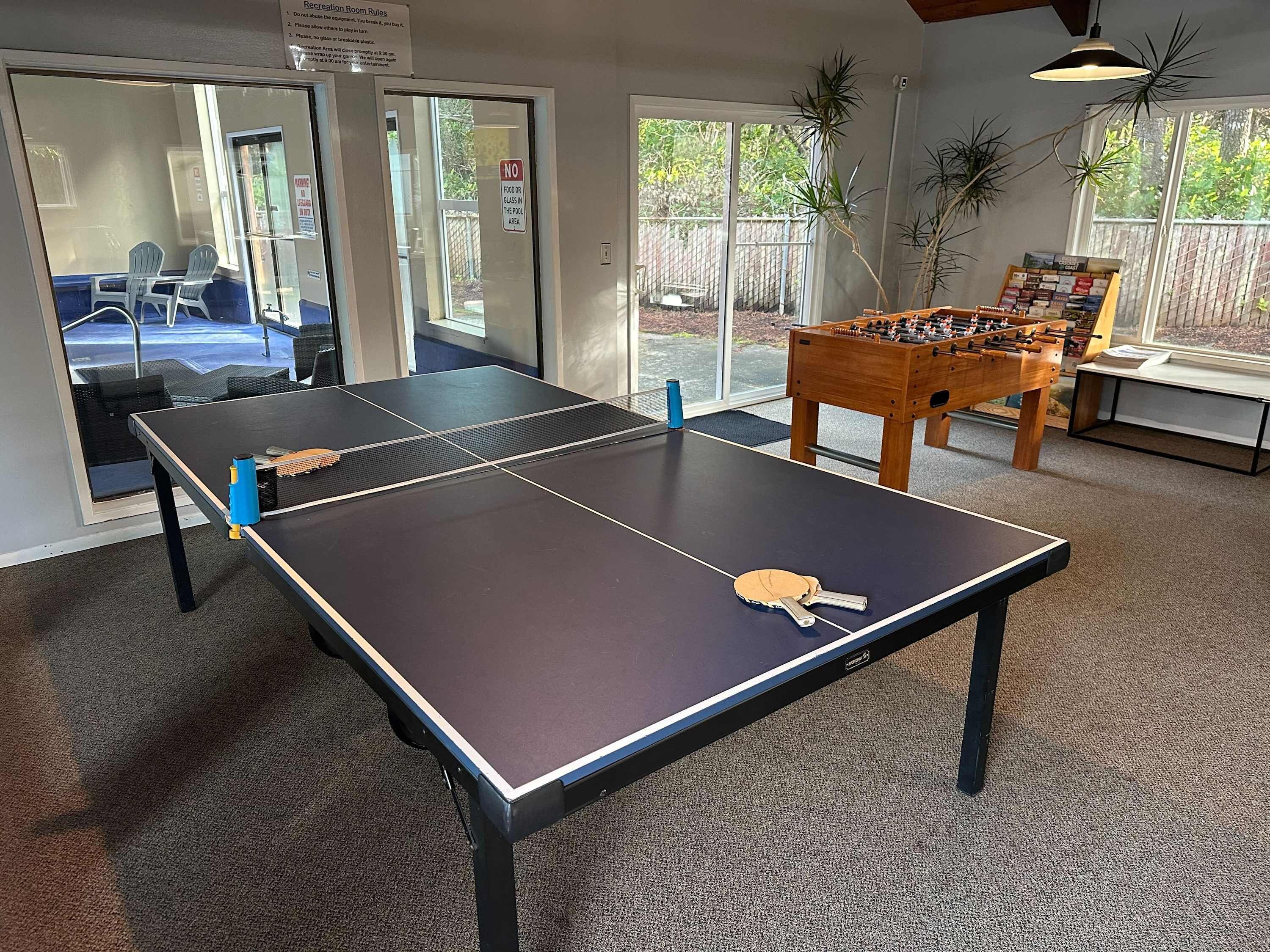 A ping pong table in a room with a foosball table and a window with a view of a backyard.