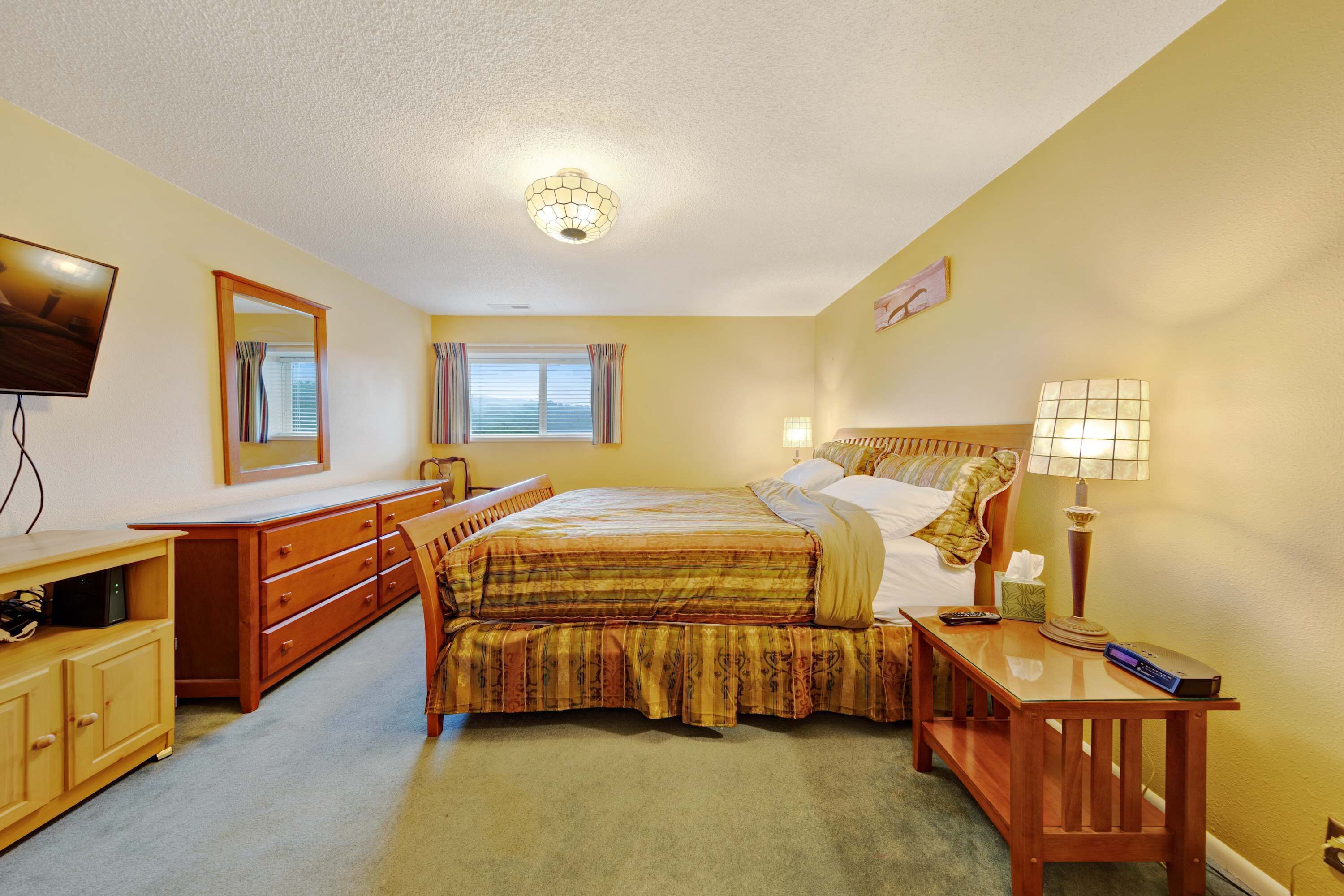 A bedroom with a bed, dresser, TV, and bedside lamp.