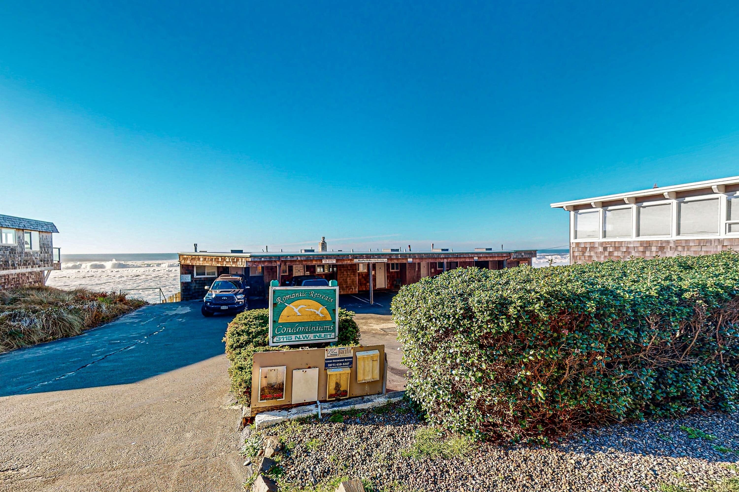 Ett hotell vid kusten med en parkeringsplats, en skylt och utsikt över stranden.
