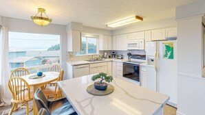 A modern kitchen with white cabinetry, a dining area with a wooden table and chairs, and a view of the outside. - Cozy house close to beach hot tub and ocean views (Lincoln City)