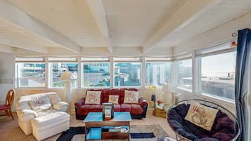 A spacious living room with a large window, a red sofa, a white armchair, and a black bean bag chair.