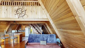 Un dormitorio de buhardilla acogedor con techo inclinado de madera, una carabela rústica, un sofá y una zona de cocina con microondas.