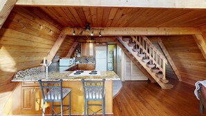 Una cocina estilo altillo con techo de madera, una isla central con taburetes de bar y una escalera que lleva a un nivel superior.