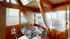 Una habitación con paneles de madera, una mesa de vidrio y sillas de metal, ventanas amplias con persianas y vistas a una terraza y valla de madera.