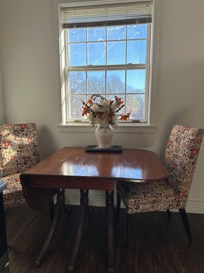 A dining table with a vase of flowers, two patterned chairs, and a window with blinds.