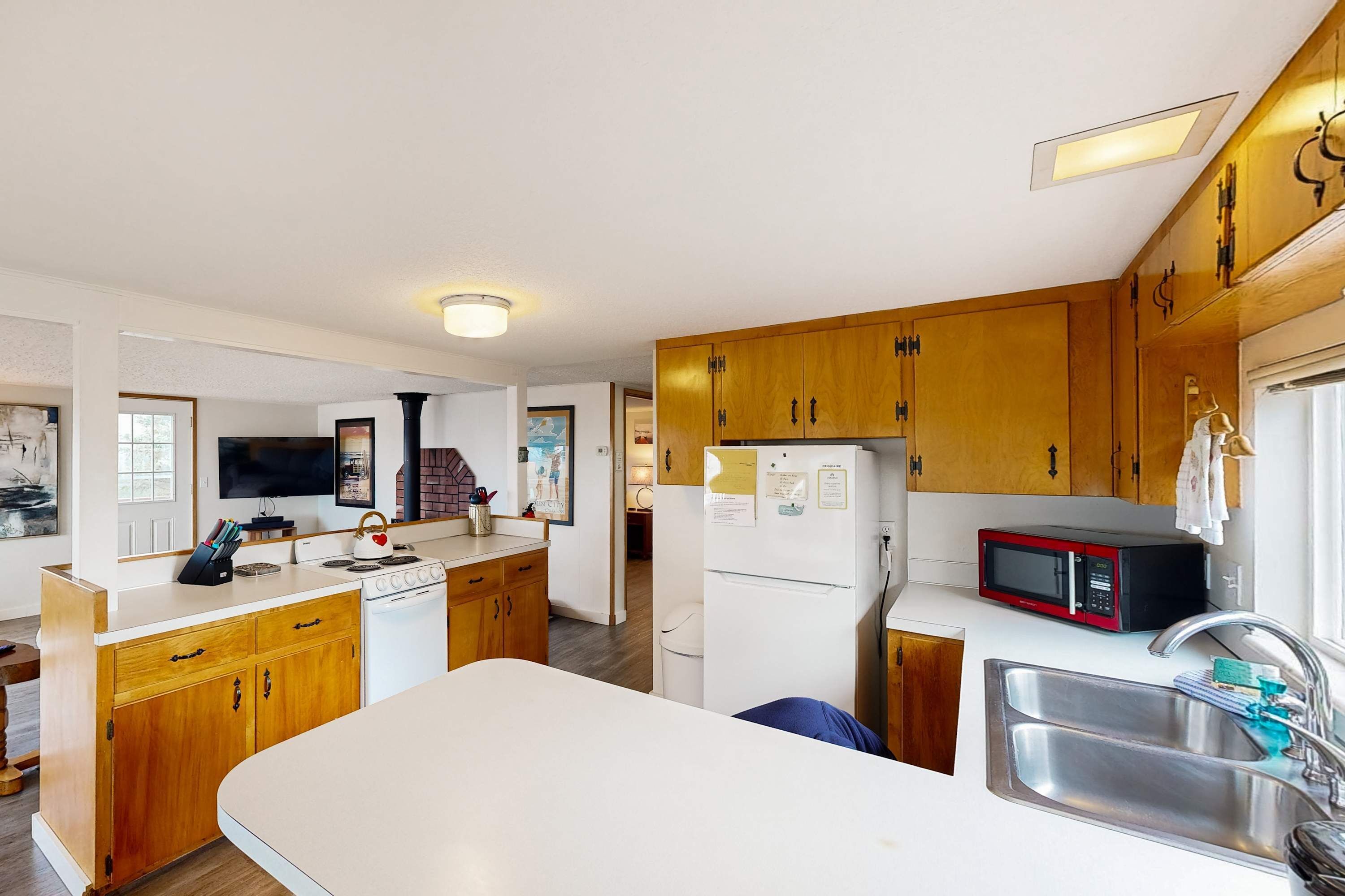 A compact kitchen with wooden cabinets, a white countertop, a microwave, a sink, and a refrigerator.