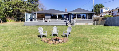 Ein Haus mit einer überdachten Terrasse, einer Feuerstelle und drei Adirondack-Stühlen.