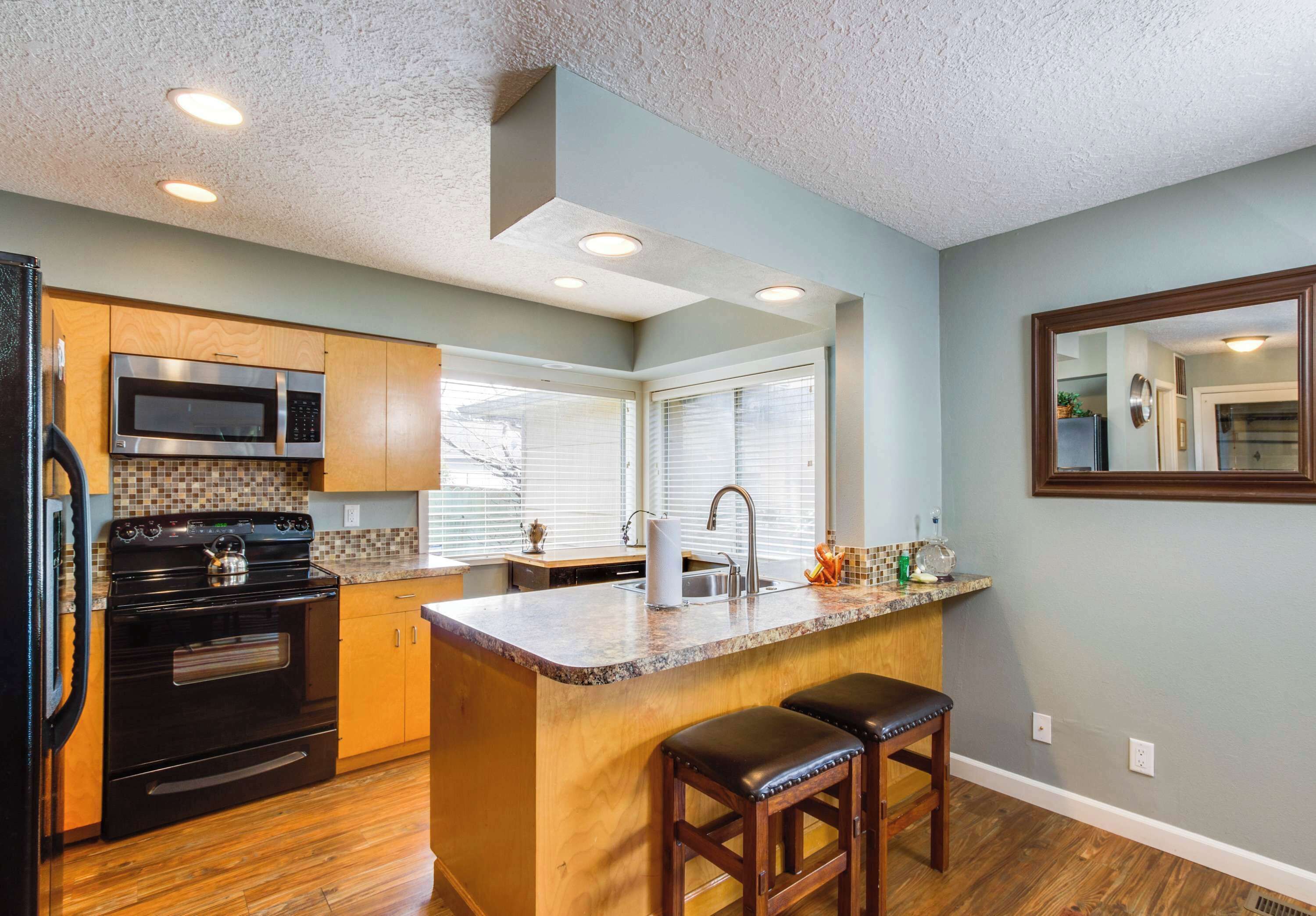 A kitchen with a central island, wooden cabinets, a black stove, a microwave, and a sink.