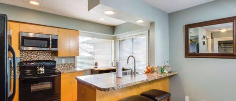 A kitchen with a central island, wooden cabinets, a black stove, a microwave, and a sink.