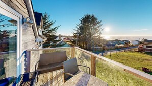 Une terrasse en bois avec une balustrade en verre, un espace salon extérieur et une vue sur une pelouse et des maisons situées au loin.