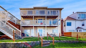 A multi-story residential building with a balcony on the second floor, a staircase on the left, and a picnic table in the front yard. - Lower Level Studio with Ocean Views and Easy Beach Access Dog Friendly (Lincoln City)