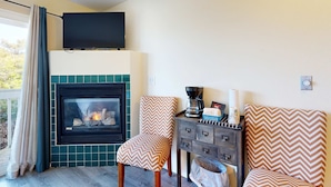 A cozy living room with a fireplace, two patterned chairs, a coffee maker, and a television on the wall. - Lower Level Studio with Ocean Views and Easy Beach Access Dog Friendly (Lincoln City)