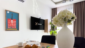 Ett matbord med croissanter, en vit vas med blommor och en platt-TV på väggen.