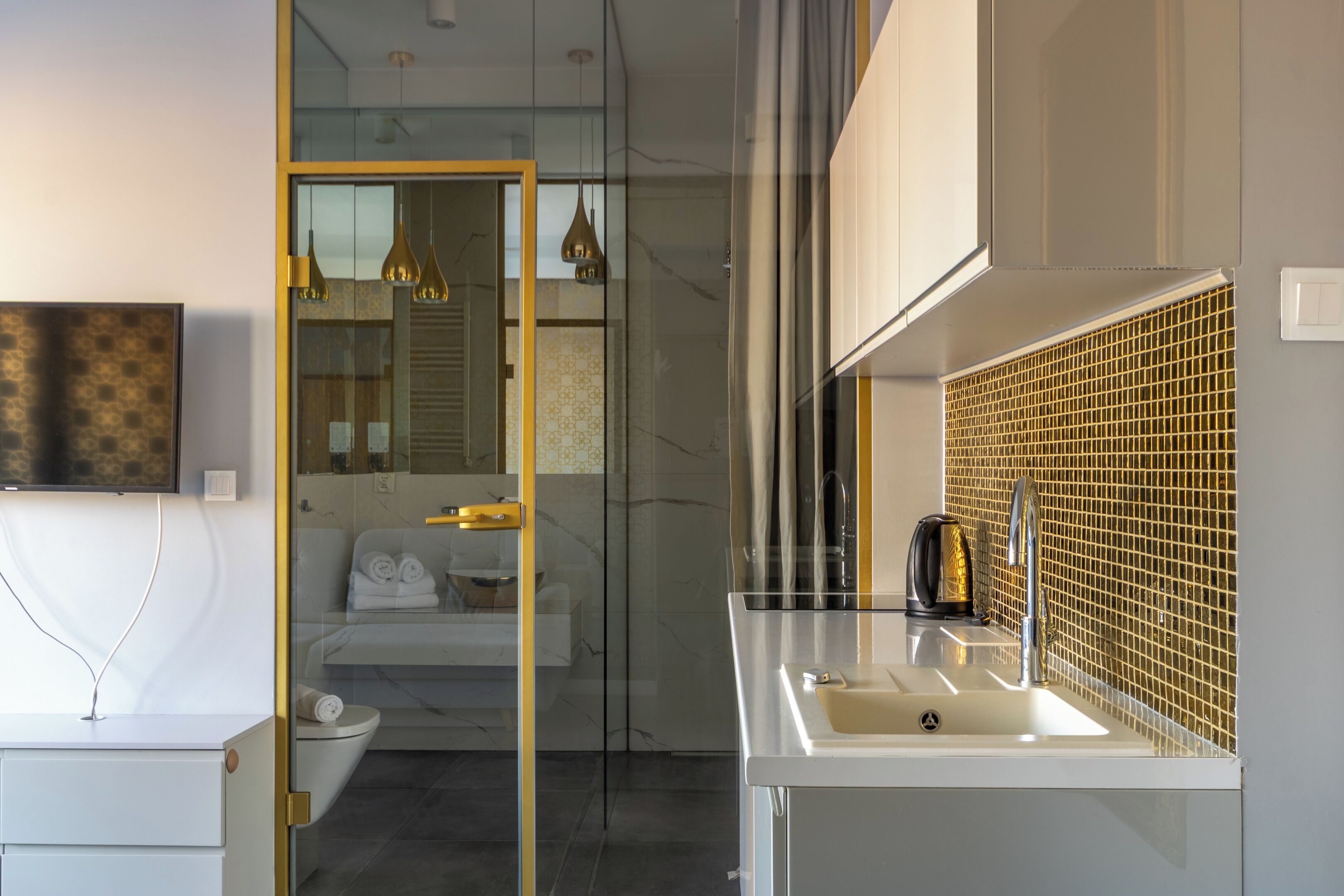 A modern bathroom with a glass shower enclosure, a white sink with a gold faucet, and a mirror with a gold-tiled backsplash.