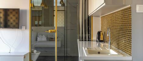 A modern bathroom with a glass shower enclosure, a white sink with a gold faucet, and a mirror with a gold-tiled backsplash.
