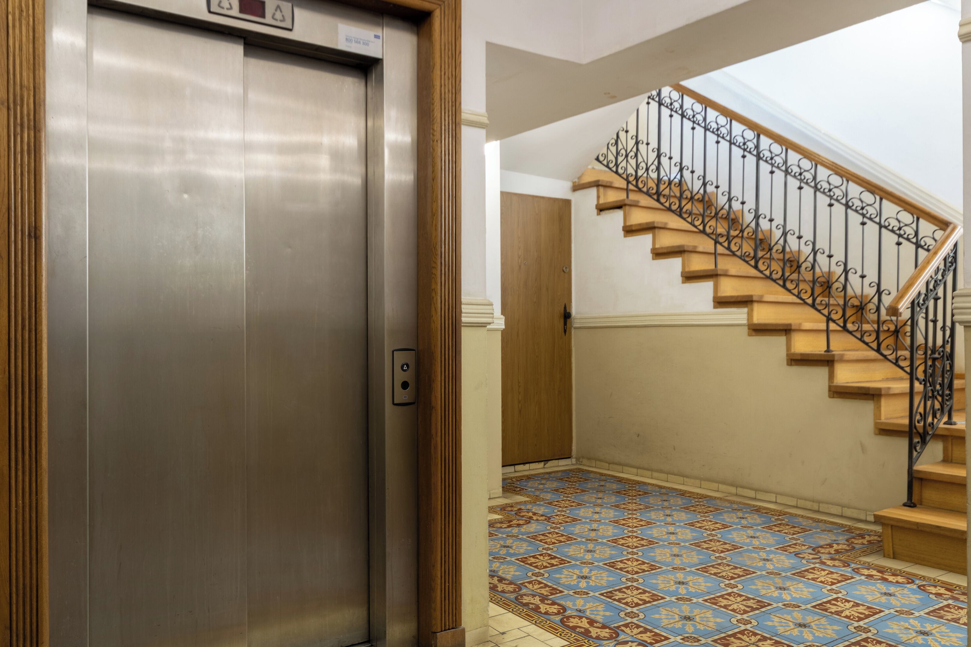 An elevator with a metallic finish, a wooden door, and a patterned floor.
