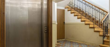 An elevator with a metallic finish, a wooden door, and a patterned floor.