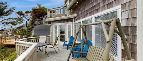 A wooden deck with outdoor furniture, including chairs and a bench, and a swing set.