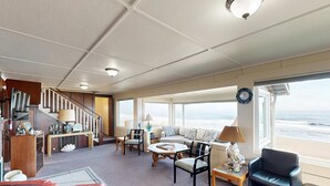 Een ruime woonkamer met een bank, stoelen, een salontafel en uitzicht op de oceaan.