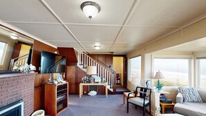 Een ruime woonkamer met een open haard, een houten tv-meubel, een trap en een groot raam met uitzicht.