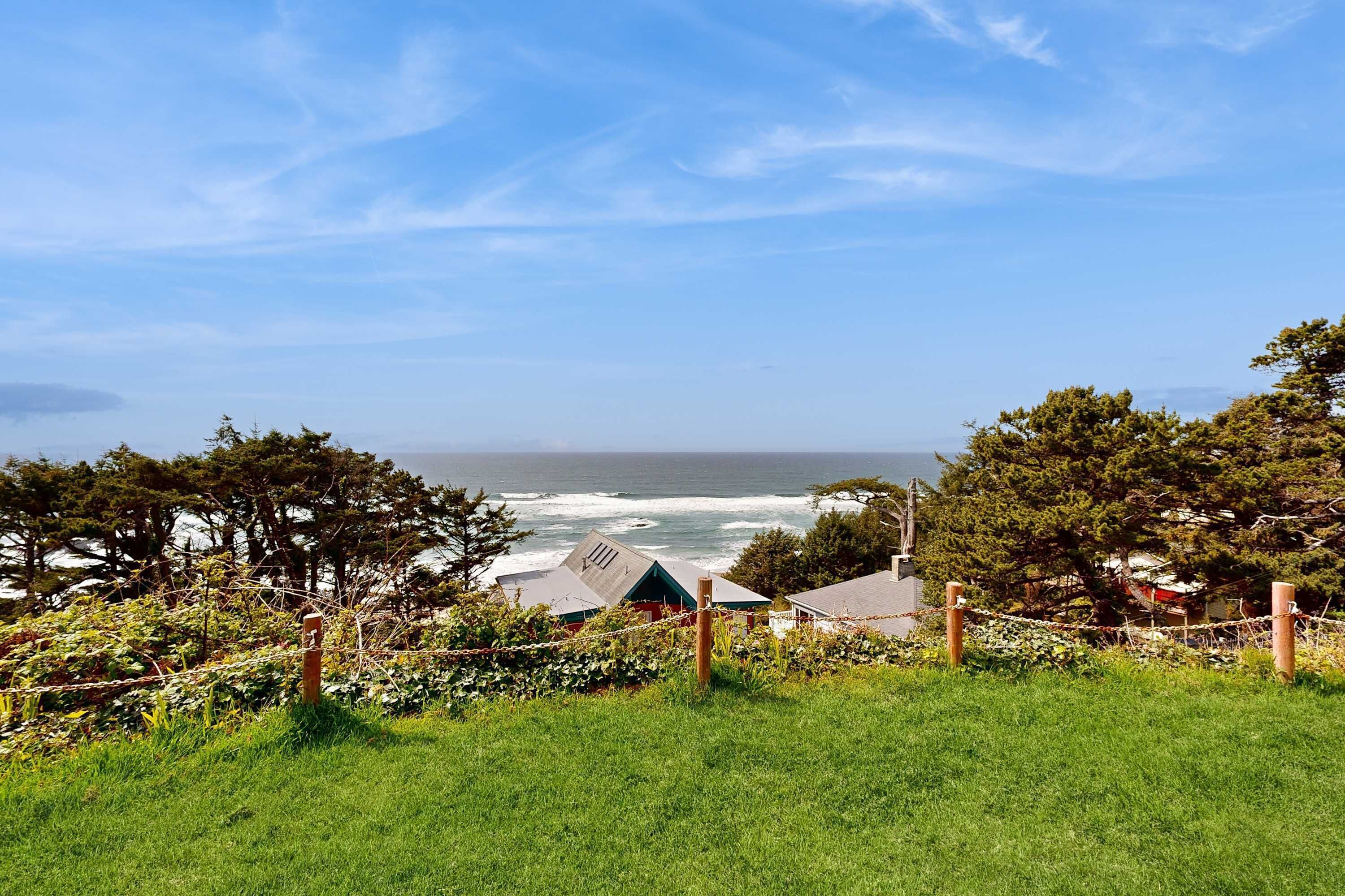 A coastal view with a grassy foreground, a wooden fence, and buildings in the background.