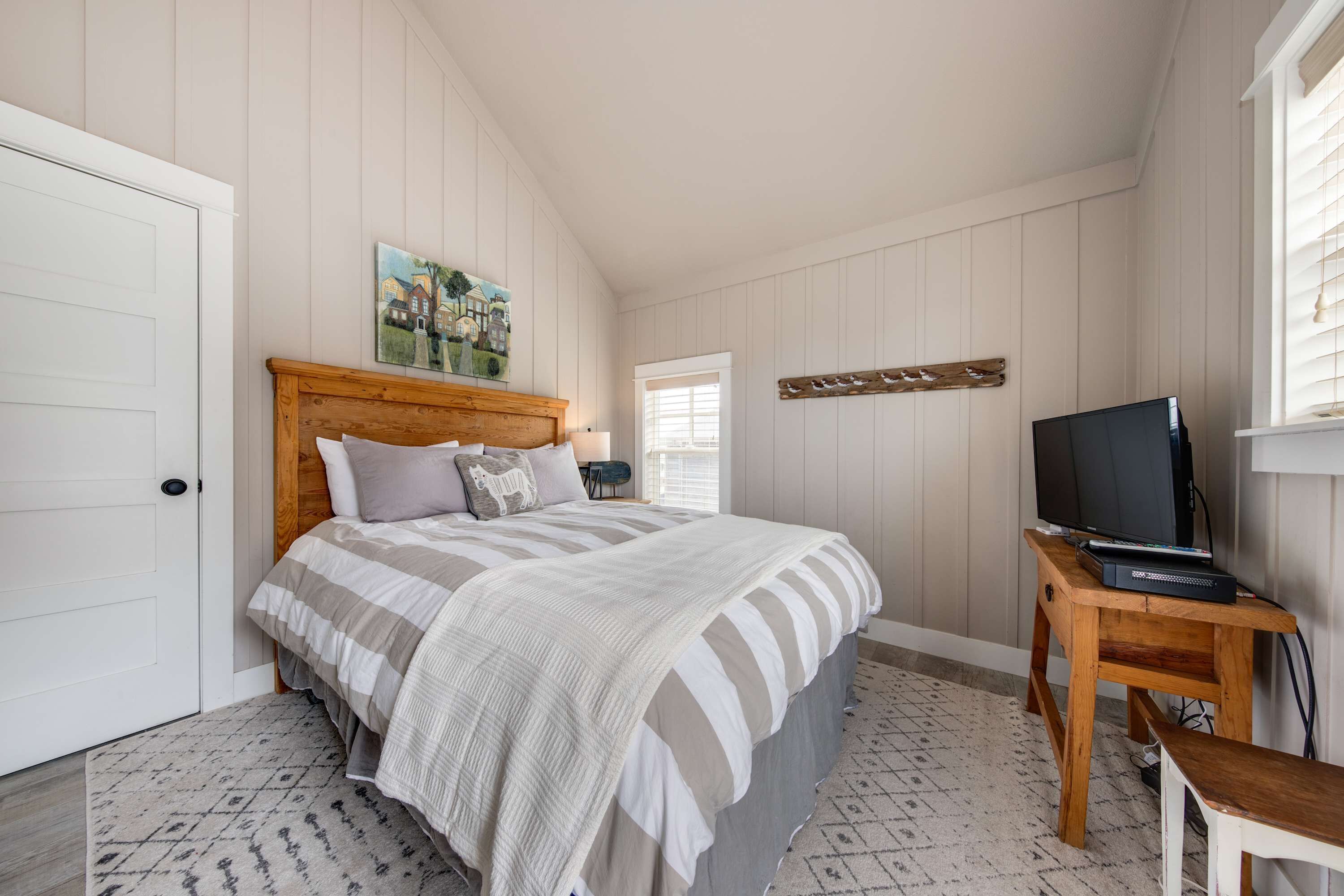 Een slaapkamer met een bed, een houten nachtkastje, een televisie en een raam met jaloezieën.