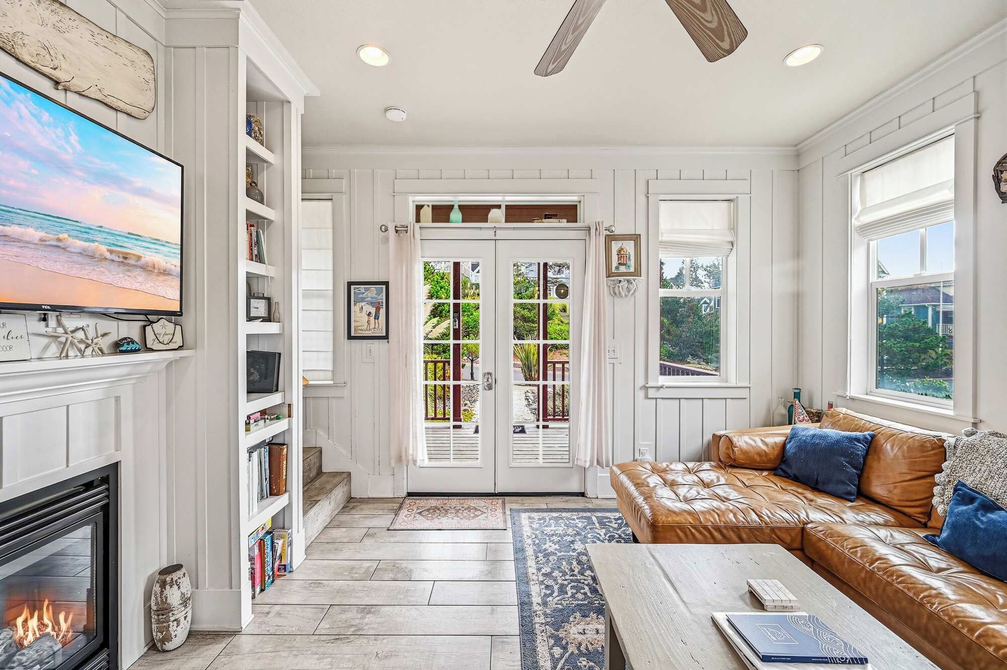A spacious living room with a fireplace, a leather sofa, a coffee table, and a television mounted on the wall.