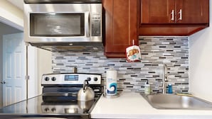 Una cocina con un microondas de acero inoxidable, una estufa, un hervidor y un lavamanos.