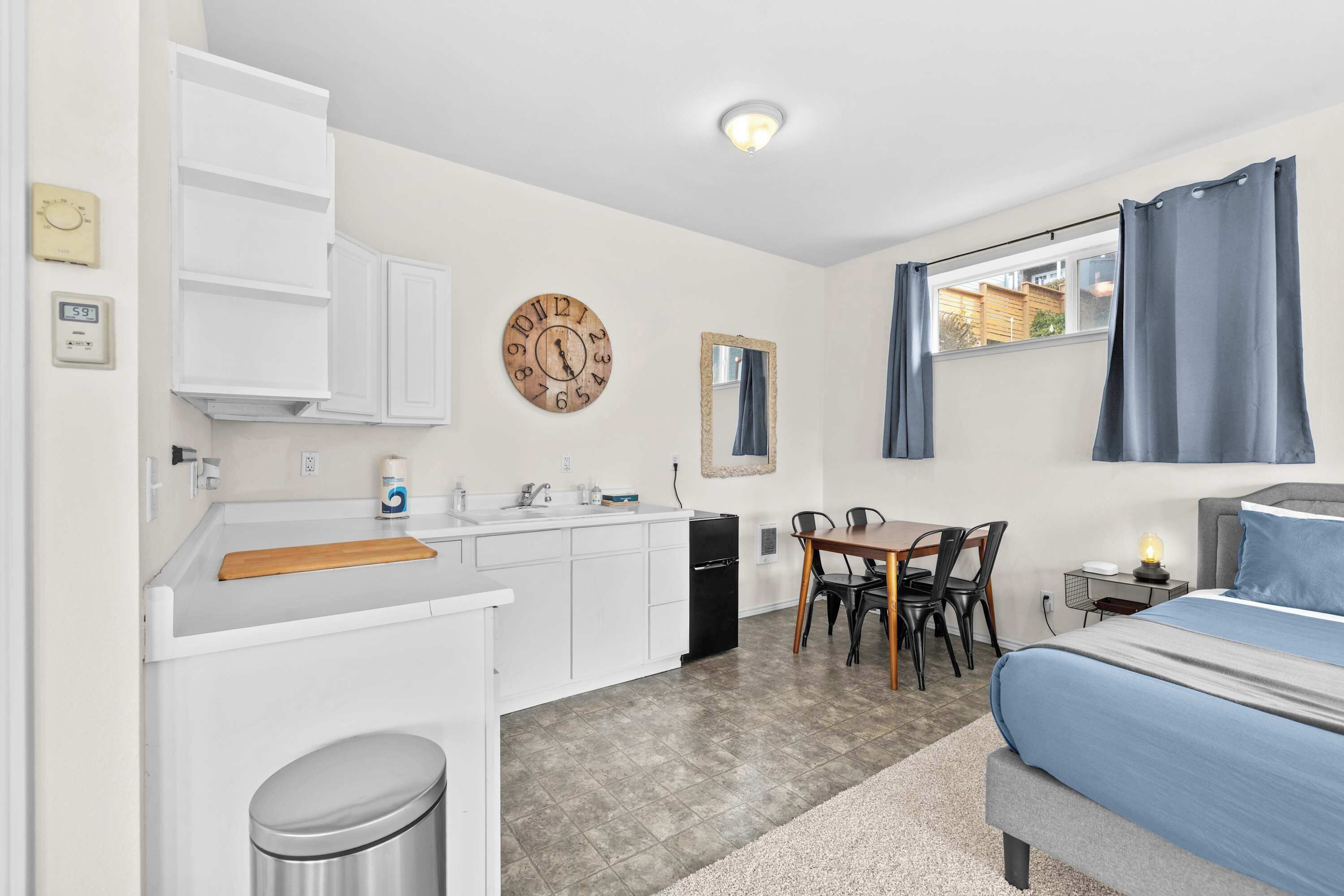 Una cocina compacta con armarios blancos, un reloj de madera y una zona de comedor con mesa y sillas.