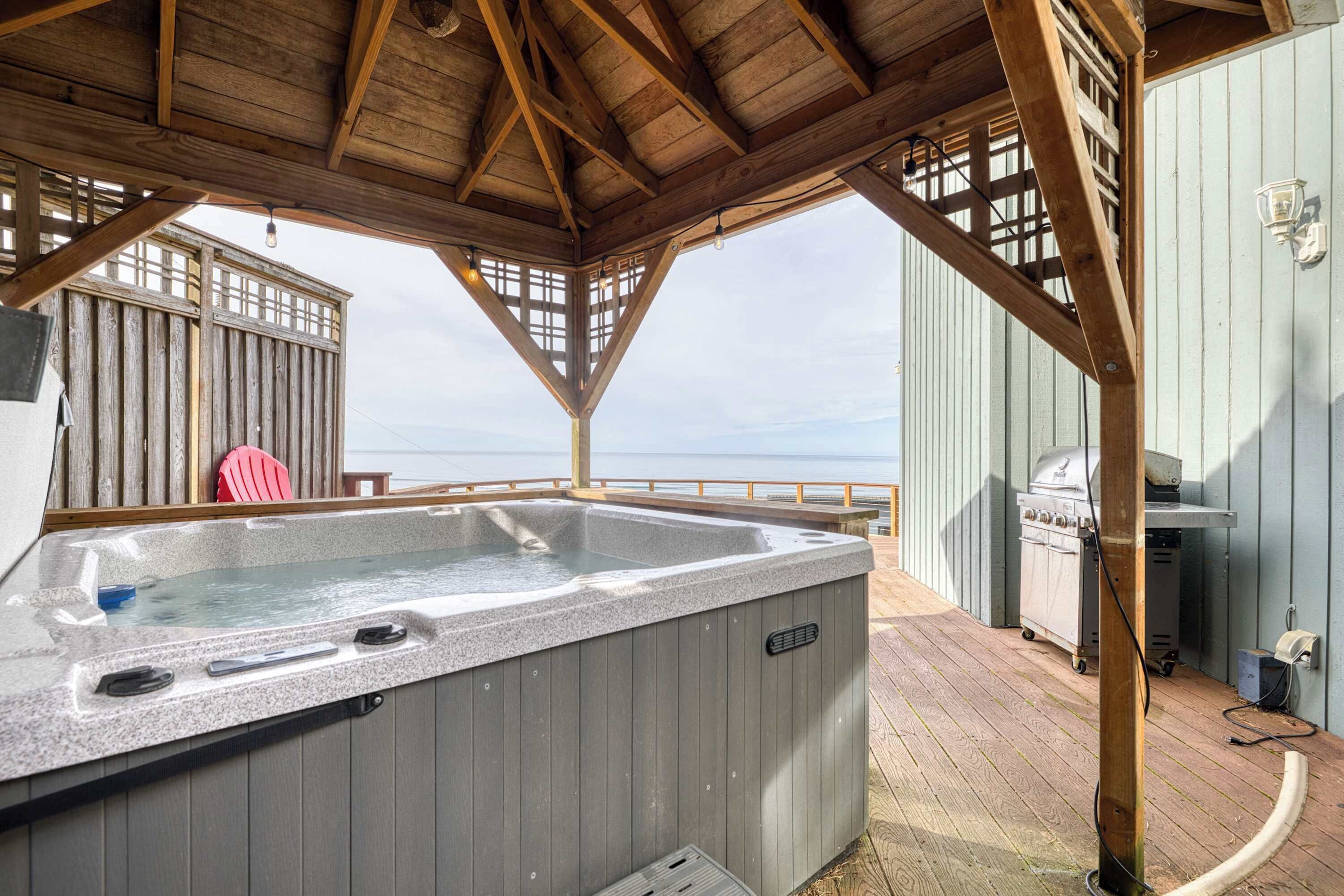 Une terrasse en bois avec un jacuzzi, un barbecue et une vue sur l’océan.