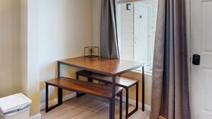 A small room with a wooden table and bench, a white trash bin, and a window with curtains. - Lovely Studio with Great View and Nearby Beach Access Dogs Welcome (Lincoln City)