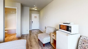 A small, compact room with a kitchenette area, a microwave, a chair, and a bed. - Lower Level Ocean View Studio Close to the Beach Dogs Welcome (Lincoln City)