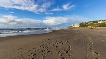 A sandy beach with footprints leading to the water, a clear sky, and buildings in the background.