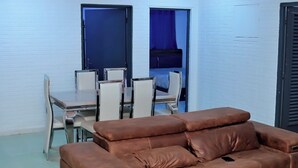 Una habitación con un sofá de cuero marrón, una mesa de comedor con sillas y una cama con cortina azul.
