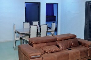 Una habitación con un sofá de cuero marrón, una mesa de comedor con sillas y una cama con cortina azul.