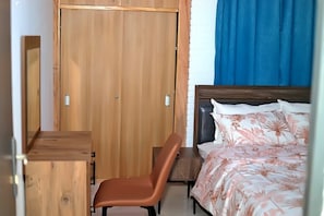 Un dormitorio con un armario de madera, una cama individual con ropa de cama floral y una silla marrón.