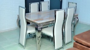 Un comedor con una mesa rectangular y seis sillas de estructura metálica y asientos acolchados.